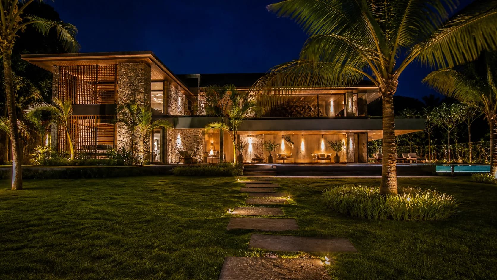 Fachada da residência iluminada à noite com paisagismo tropical